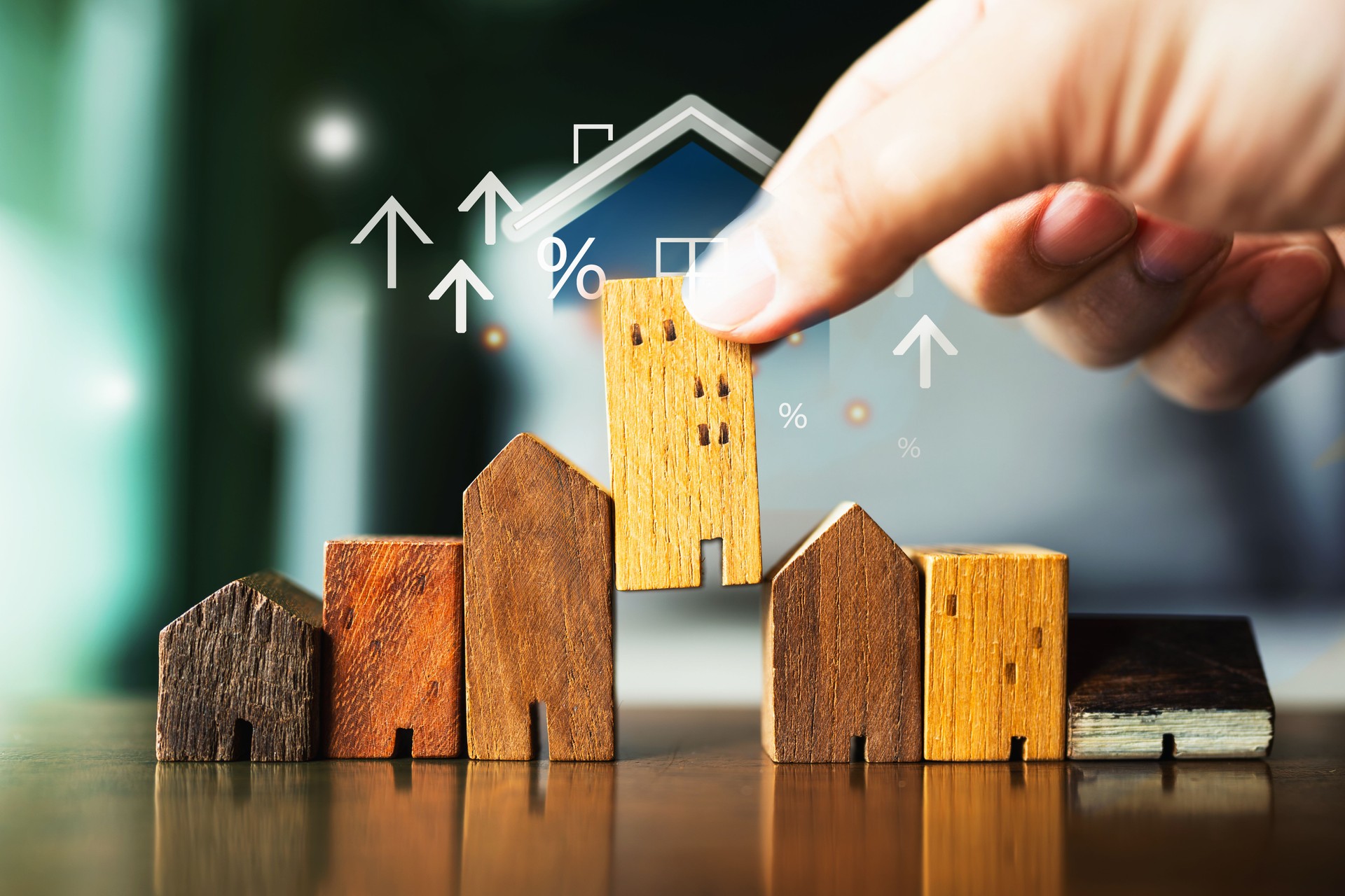 A hand selects a model house on a table, surrounded by graphics of arrows, dollar signs, and percentages. This vividly illustrates the strategic process of selecting and investing in real estate.